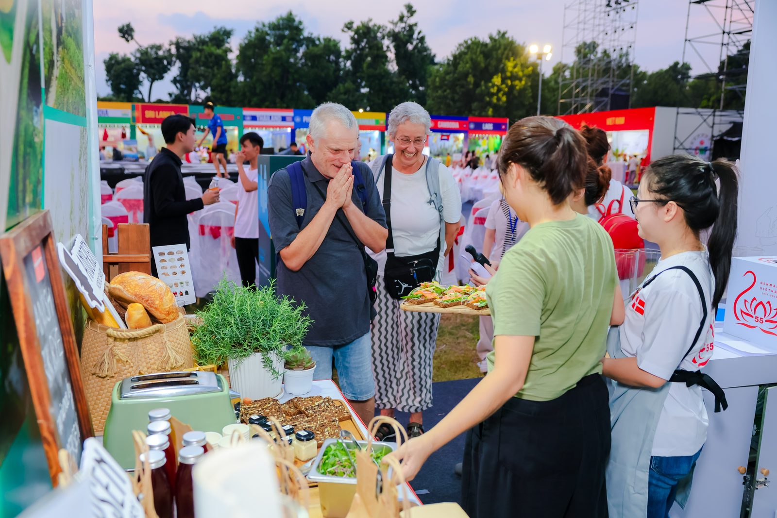 Two visitors smile as the Andersen team serves open sandwiches at the booth